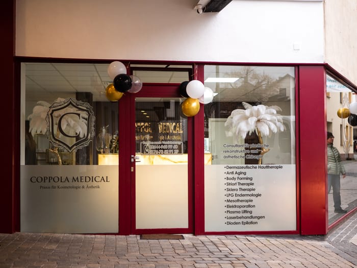 Eingang von Coppola Medical mit roten Rahmen und goldenem Wappen in der Scheibe